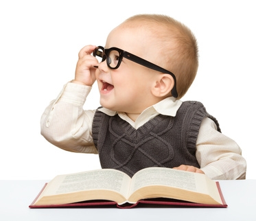 Cute little child play with book and glasses while sitting at table, isolated over white